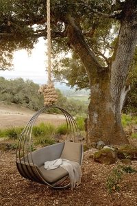 Металлические качели оригинальной формы, подвешенные к ветке дерева с помощью веревки Металлические качели оригинальной формы, подвешенные к ветке дерева с помощью веревки