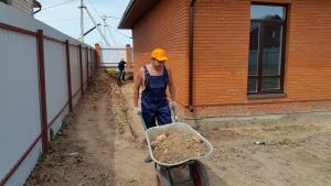 Процесс строительства отмостки вокруг дома: выкапывание траншеи Процесс строительства отмостки вокруг дома: выкапывание траншеи